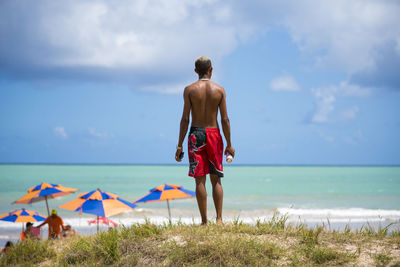 Rear view of shirtless man looking at sea against sky