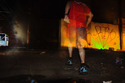 Low section of man standing by illuminated light at night