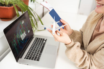 Woman holding toy plane, tickets, laptop and taxes