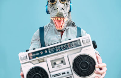 Midsection of man wearing mask while holding radio while standing against blue background