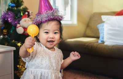 Portrait of smiling girl wearing party hat while holding toy at home