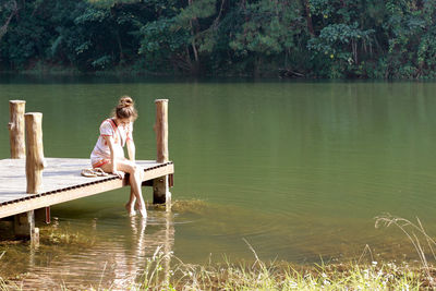 Woman sitting by lake against trees