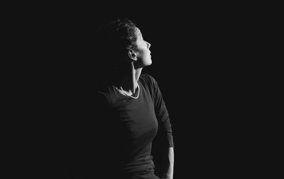 Side view of young man looking away against black background
