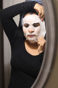 Woman removing facial mask reflecting in mirror