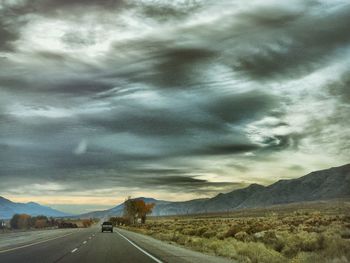 Road passing through landscape against storm clouds