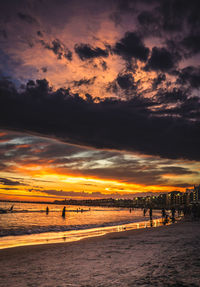 Scenic view of beach against dramatic sky during sunset