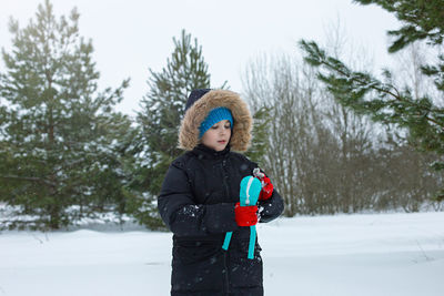 A boy sits in the snow, makes snowballs using a light blue plastic sculpting tool