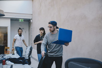 Computer programmer holding laptop while walking with colleagues in office