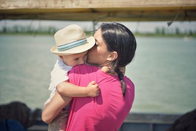 Mother kissing son against lake