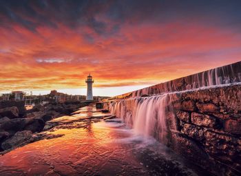 Water falling from stone wall during sunset