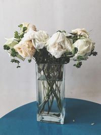 White roses in glass jar on table against wall