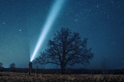 Man with flashlight standing against star field on field