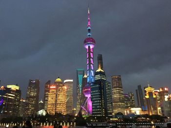 Low angle view of illuminated oriental pearl tower amidst buildings in city at dusk