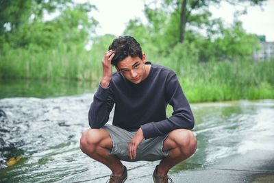 Young man sitting by lake against trees