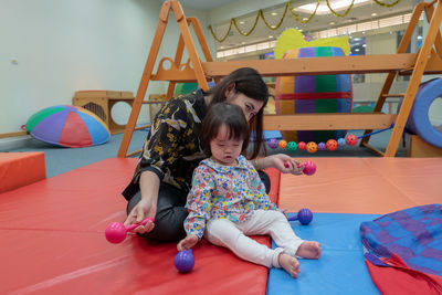 Cute girl with teacher playing on carpet in kindergarten