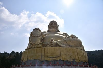Low angle view of large gold statue at thousand buddha mountain against sky