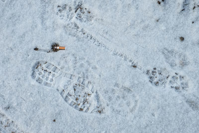 High angle view of  footprint in snow with cigarette butt