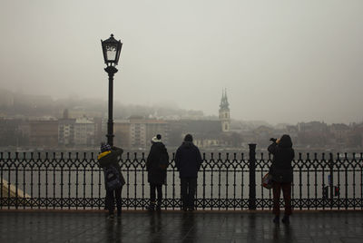 People on footbridge over river in city