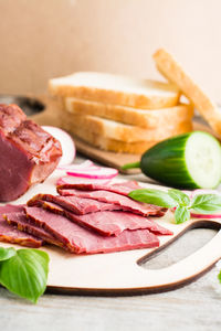 Fresh sliced marbled beef pastrami, cucumber, radish and basil on a cutting board