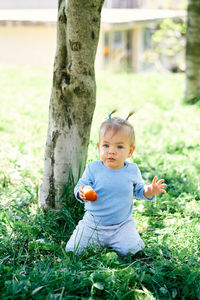 Cute boy sitting on tree trunk in field