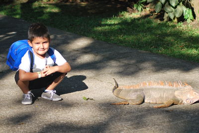 Portrait of boy crouching by iguana on road