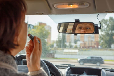 Portrait of woman photographing through car windshield