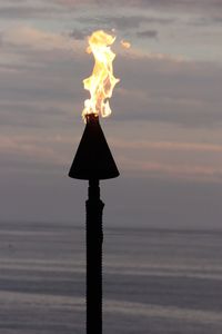 Burning oil lamp at beach against sky during sunset