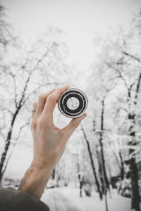 Cropped hand of person holding lens against bare tree during winter