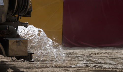 Cropped image of truck spraying water on sand
