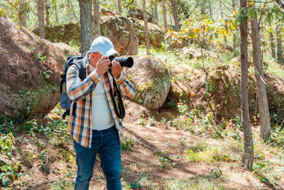 Rear view of man photographing in forest