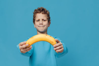 Portrait of young woman holding banana against blue background