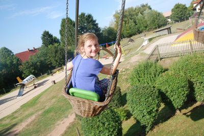 Portrait of smiling girl swinging at playground during sunny day