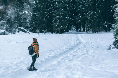 Woman in winter clothes standing on snowy path leading to moody forest