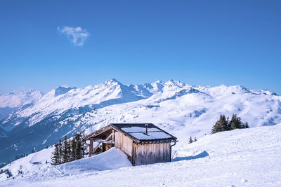 Small wooden house on snowy mountain against blue sky