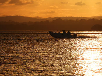 Silhouette boat in sea against orange sky