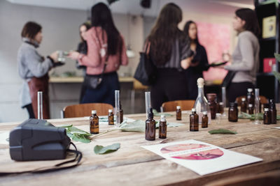 Perfume bottles on table against multi-ethnic female colleagues eating lunch while standing at workshop