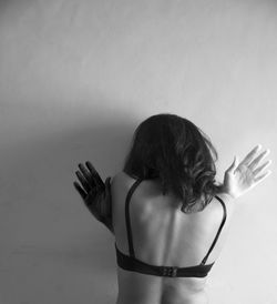 Rear view of woman wearing bra standing against wall