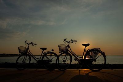 Bicycle parked by sea against sky during sunset