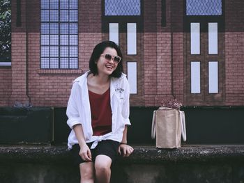 Happy young woman sitting on window against brick wall