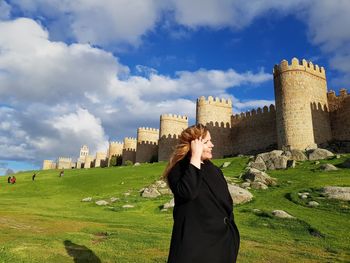 Woman standing on historical building against cloudy sky