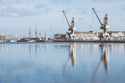 Cranes at harbor against sky