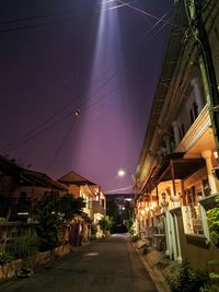 Illuminated street amidst buildings against sky at night