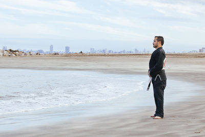 Side view of man standing on beach against sky