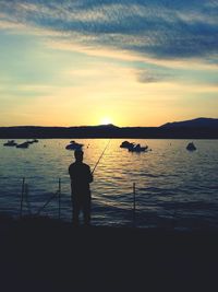 Silhouette man fishing in sea against sunset sky