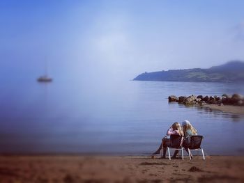 People sitting on beach by sea against sky