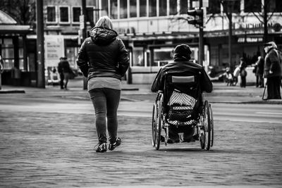 Rear view of woman walking by man on wheelchair at walkway