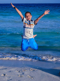 Full length portrait of happy boy jumping at beach
