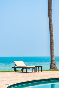 Chair by swimming pool against clear sky