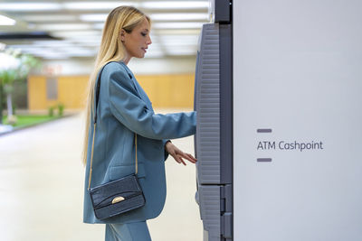 Blond working woman using atm at subway station