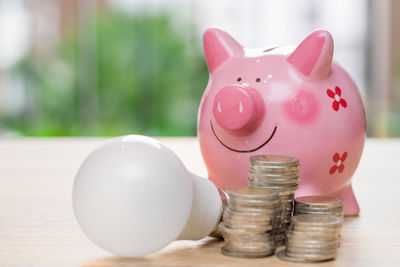 Close-up of coins by light bulb and piggy bank on table